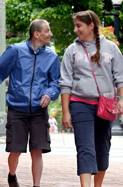 image: A father walks alongside his daughter both in casual attire as they smile at each other