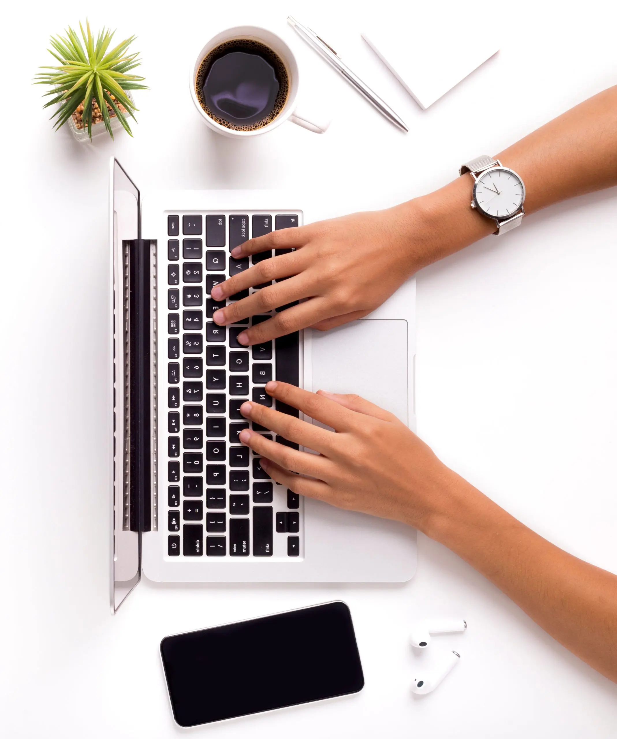 image: hands typing in a laptop above a table with a coffee mug, airpods, a cellphone and a succulent